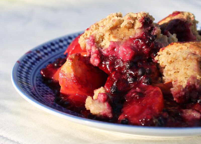 A serving of Blackberry Peach Cobbler on a blue plate on a white cloth