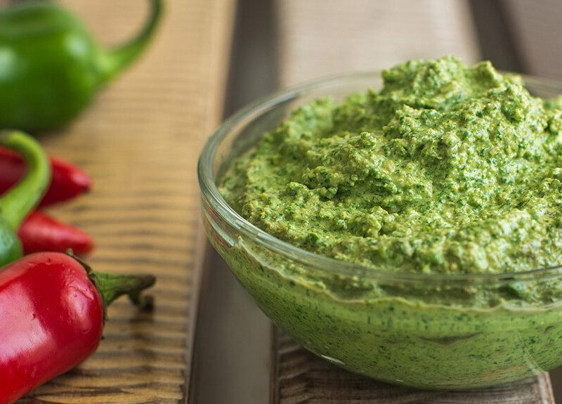 A small glass bowl of Spicy Cilantro Pesto next to fresh green and red chiles