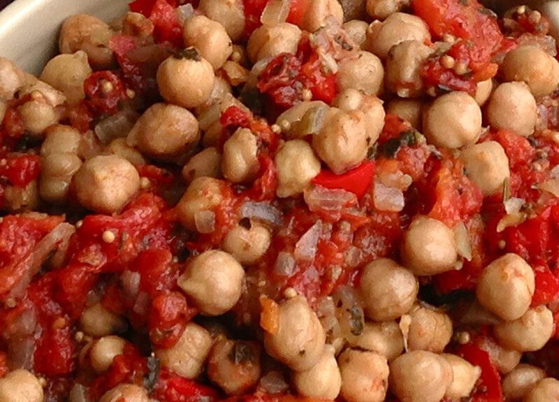A closeup of Oven-Baked Chickpea Ratatouille in a red bowl with a cloth napkin in the background