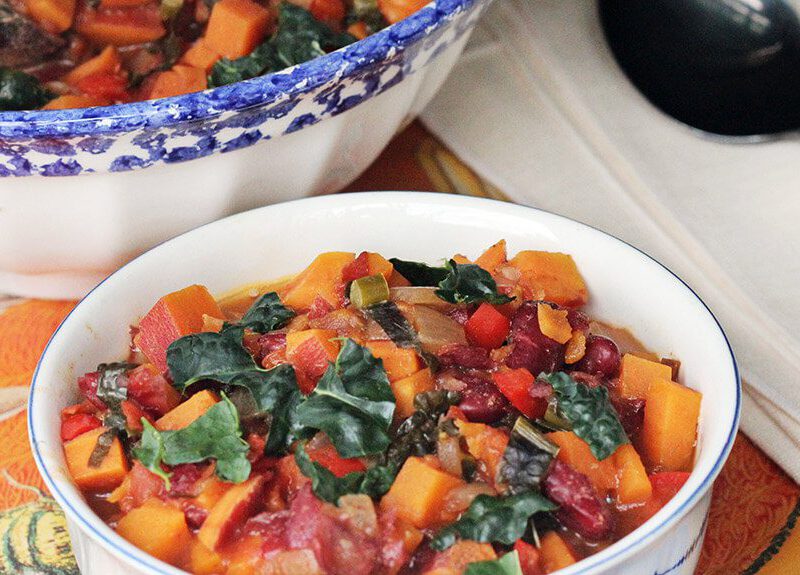 A smaller white bowl of Sweet Potato Chili with Kale next to a larger bowl and a spoon and napkin