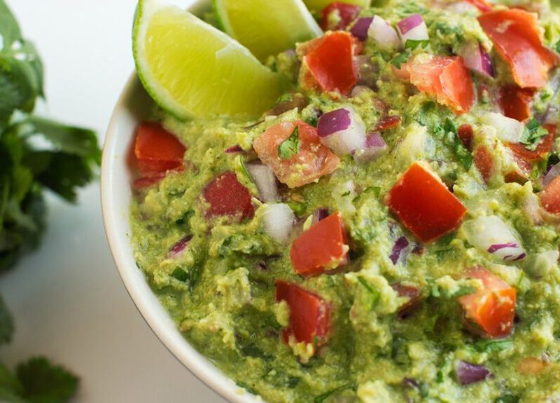 Not-So-Fat Guacamole with lime wedges in the bowl, next to a bunch of fresh cilantro