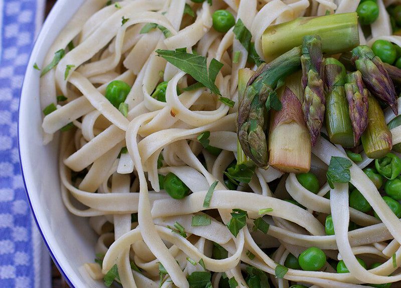 Fettuccine with Grilled Asparagus, Peas, and Lemon in a white bowl with a fork to one side