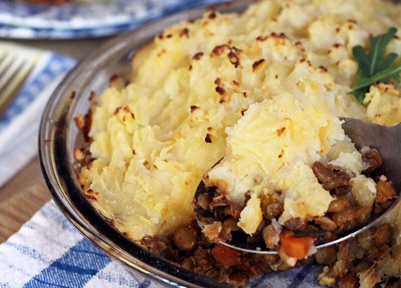 A casserole dish filled with Lentil Shepherd's Pie, with one spoonful being served up.
