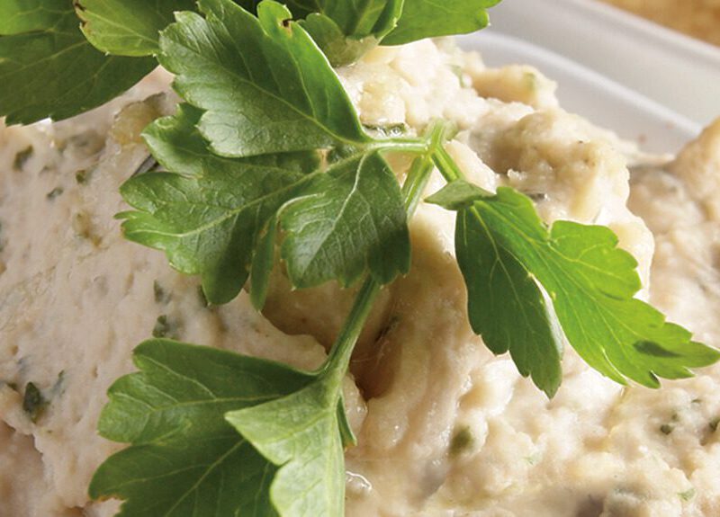 White Bean Hummus with Fresh Thyme and Basil in a white bowl with a sprig of flat-leaf parsley on top