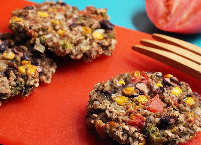 Three Plant-Based Rainbow Veggie patties on a red chopping board with a wooden serving fork