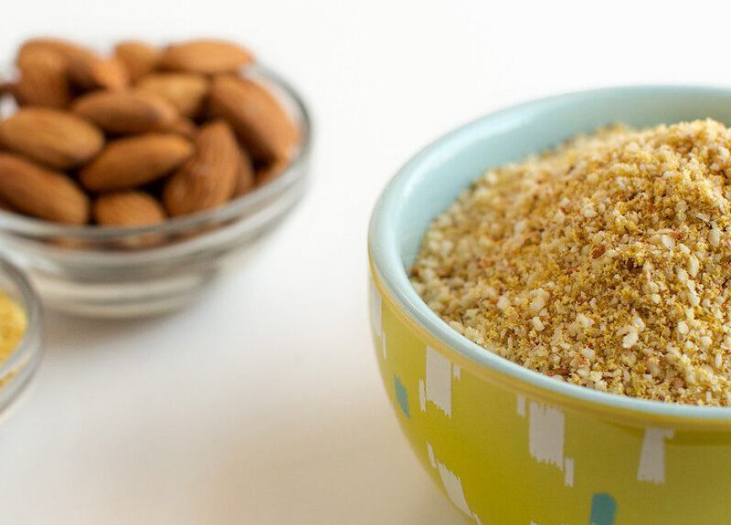 Faux Parmesan in a small colorful yellow bowl next to two smaller pinch bowls of nutritional yeast and whole almonds
