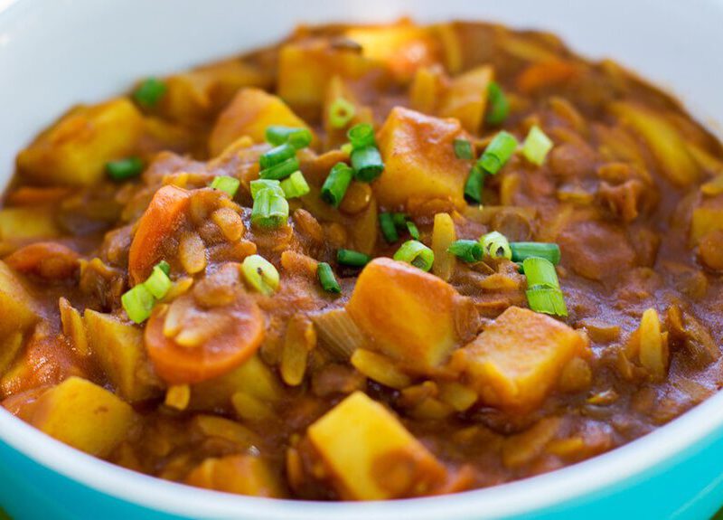 A blue bowl on a green plate filled with Curried Tomato Lentil Soup (Shorba Addis)