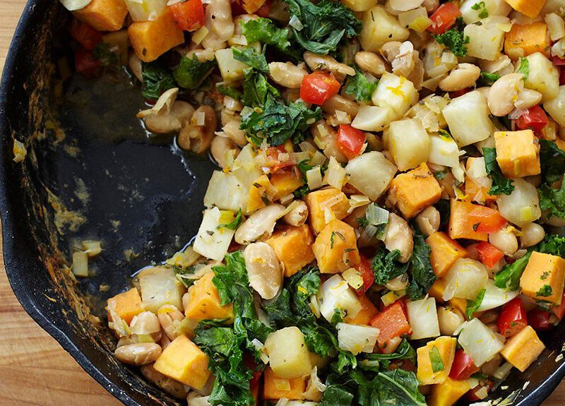 Vegetable White Bean Hash in a cast-iron skillet on a wooden chopping board