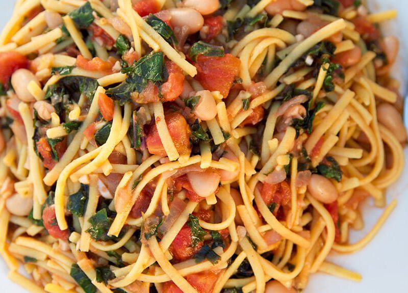 A white, square plate of White Beans with Greens, Garlic and Tomato