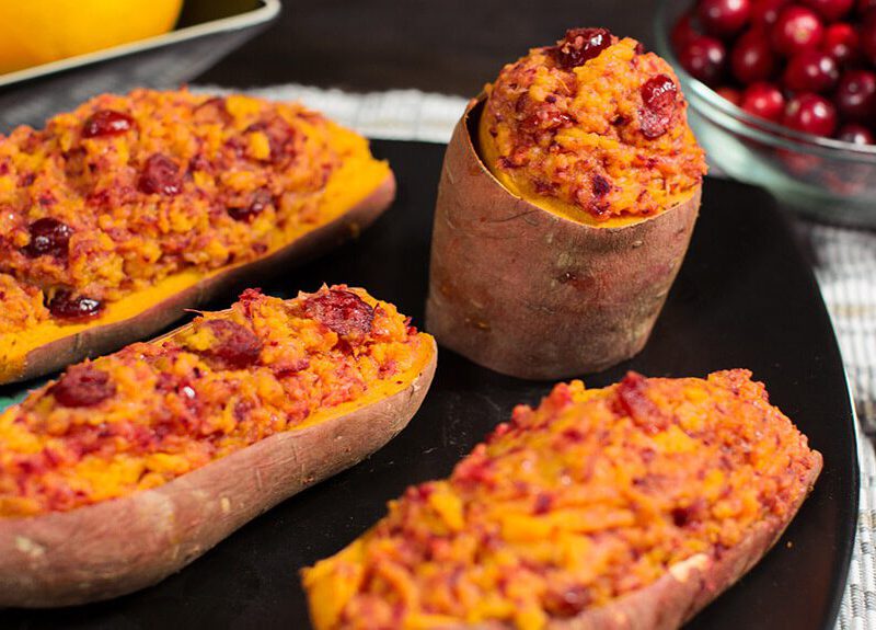 Twice Baked Sweet Potatoes on a black plate. In the background is a bowl of fresh cranberries and a bowl of oranges