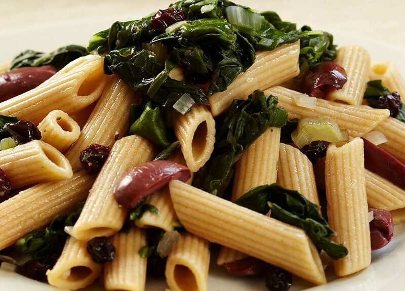 A white plate of Penne with Swiss Chard Olives and Currants