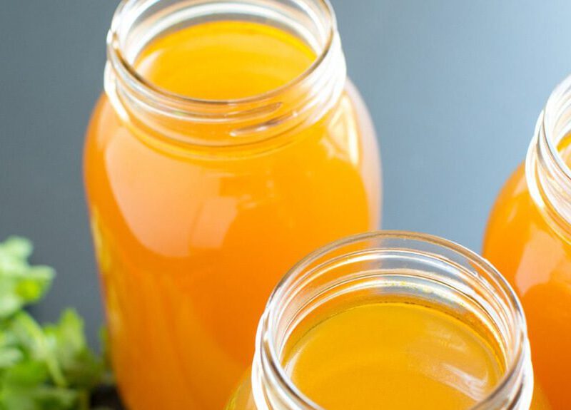 Three mason jars of orange-hued vegetable stock against a grey background