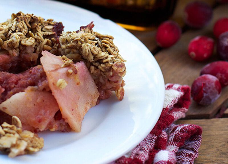 Cranberry Apple Crisp on a plate with a red and white checked cloth napkin and fresh cranberries to the side