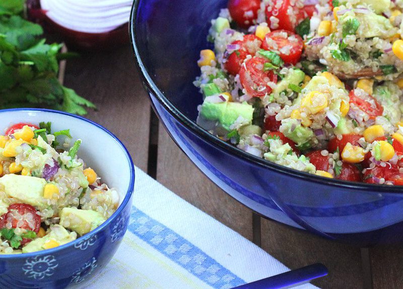 Quinoa, Corn, and Avocado Salad in a blue glass bowl with one serving in a smaller blue bowl to the side