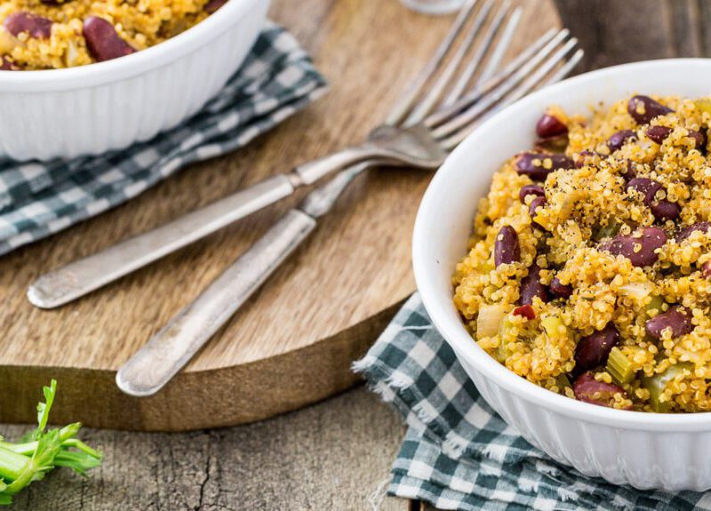 Two bowls of Red Beans and Quinoa. One bowl sits on a round wooden chopping board with a couple of forks; the other rests on a black-and-white checked napkin