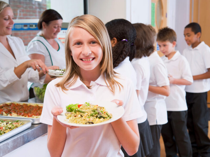 Schoolgirl holding plate of vegan lunch in school cafeteria