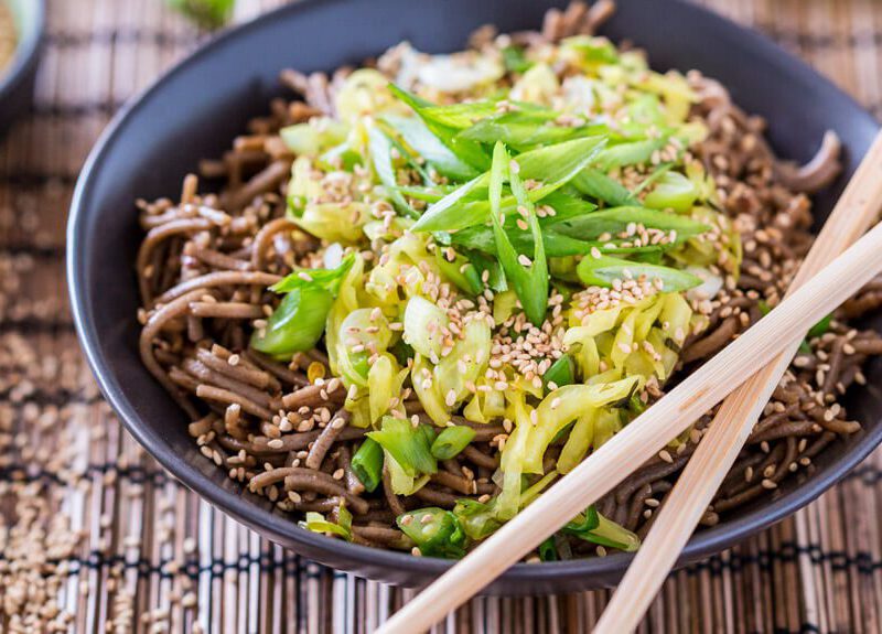 Dan Dan Mian Noodles in a black serving bowl on a grass mat with chopsticks on the bowl