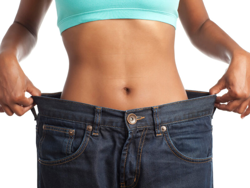 The torso of a slim women wearing pants that are miles too big for her, holding the waistband out to the sides