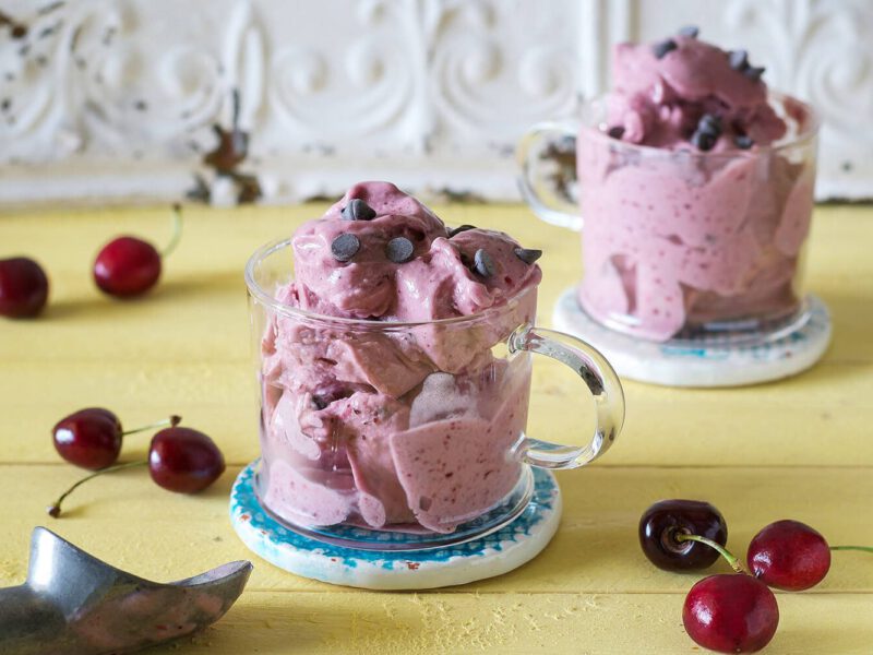 Two glass mugs of Cherry Soft-Serve Ice Cream with fresh cherries strewn on the table