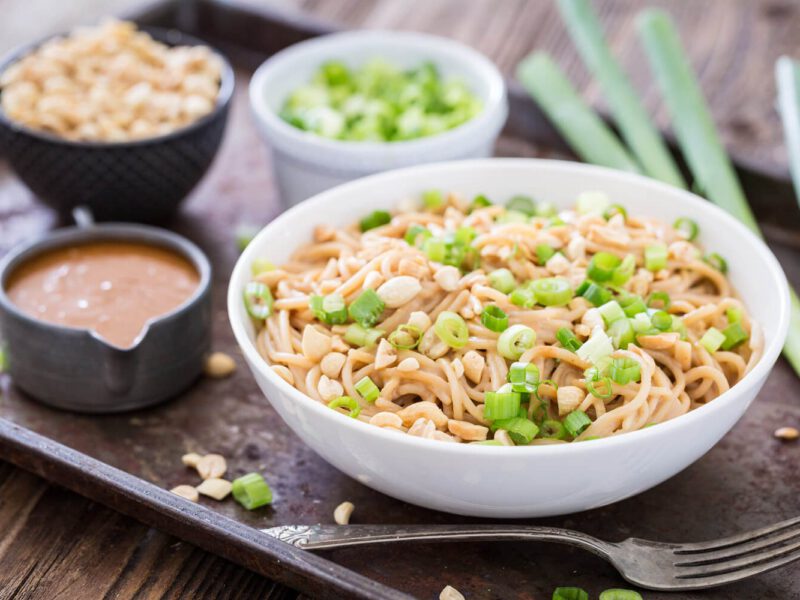 Chilled Peanut Noodles garnished with scallions and chopped peanuts, with small bowls of peanuts, scallions, and peanut sauce off to the side