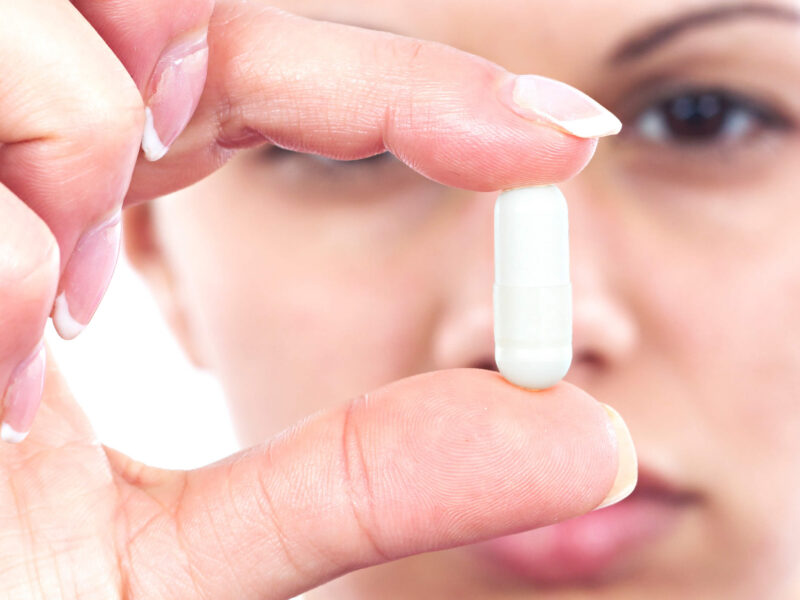 Close-up of unidentified woman holding a white capsule in front of her face