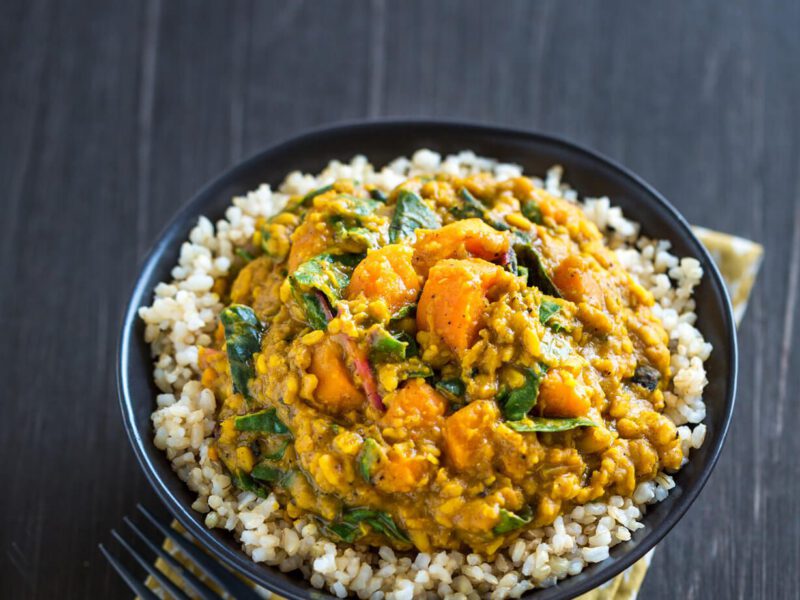 Lentil, Chard & Sweet Potato Curry atop brown rice in a black bowl