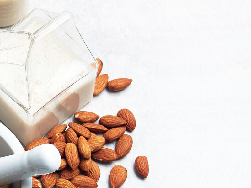 A glass carafe of nut milk next to whole almonds and a mortar and pestel