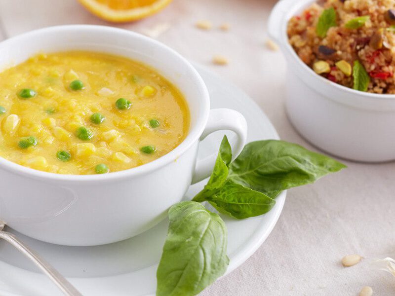 Butternut Squash Soup with Peas in a white bowl on a white plate with a sprig of basil on the side