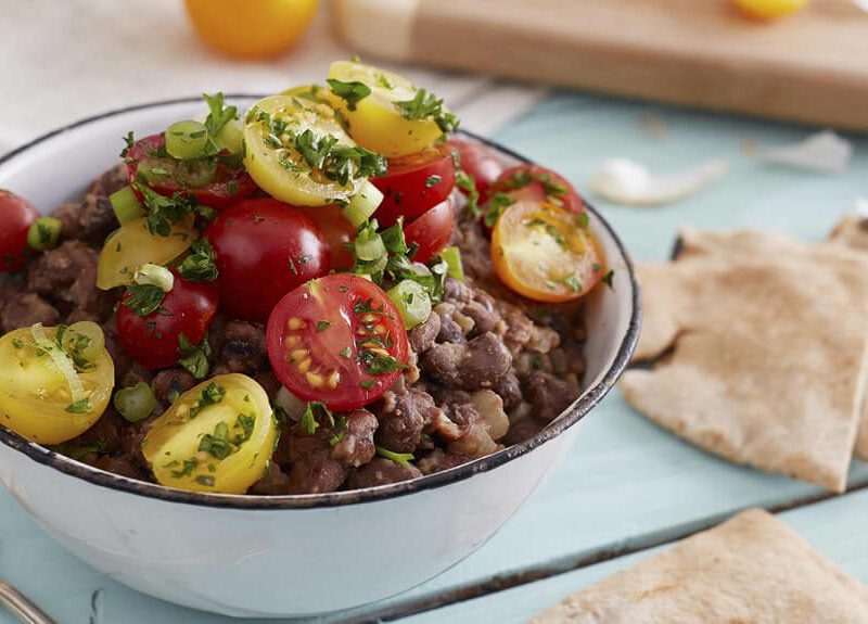 Egyptian Breakfast Beans (Ful Medames) garnished with fresh herbs with pita squares and a wedge of lemon