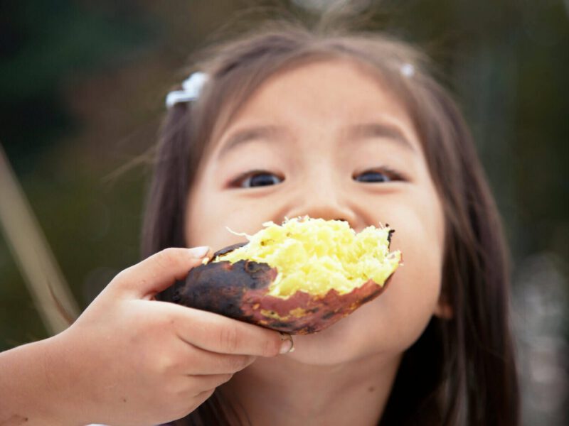 Young girl holds a large baked potato up to her face, obscuring her mouth