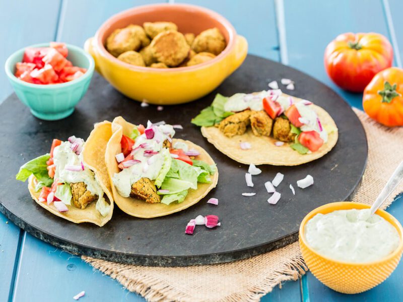 A round black baking tray with three tacos and a bowl of falafel
