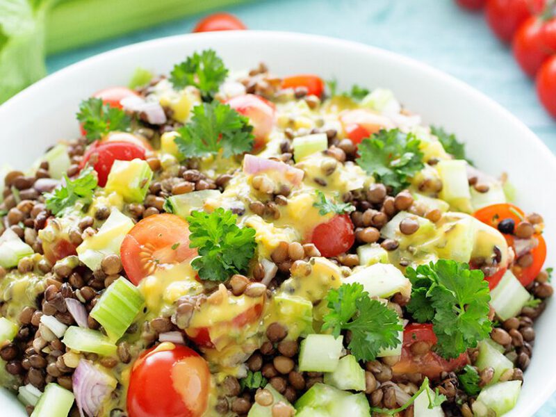French Green Lentil Salad on a pale blue wooden table with fresh tomatoes, celery, and parsley