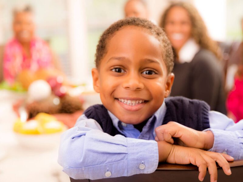 Young boy with his family in the background, looking into the camera with a big smile
