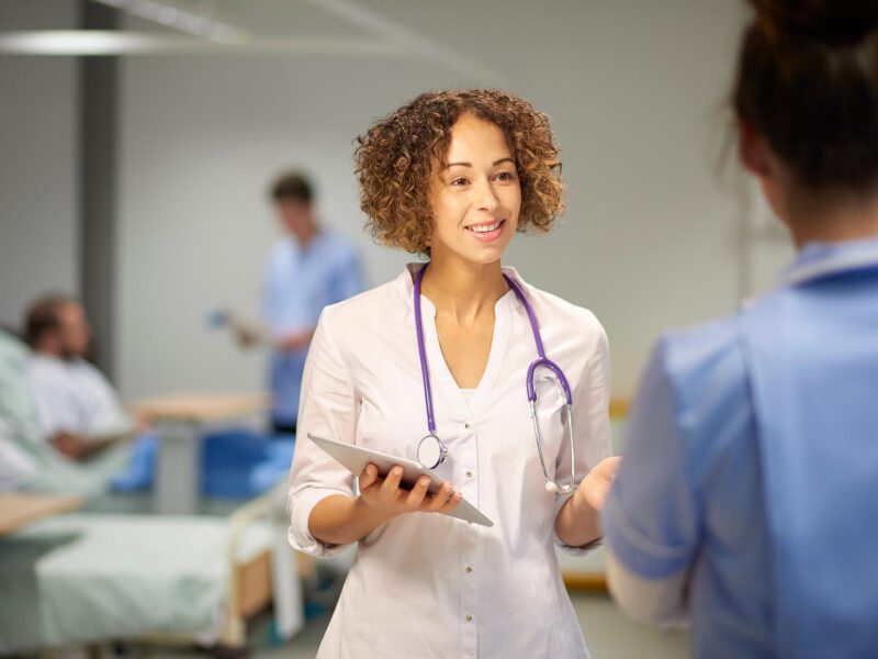 young female doctor with a stethoscope around her neck in a ward, talking to a nurse