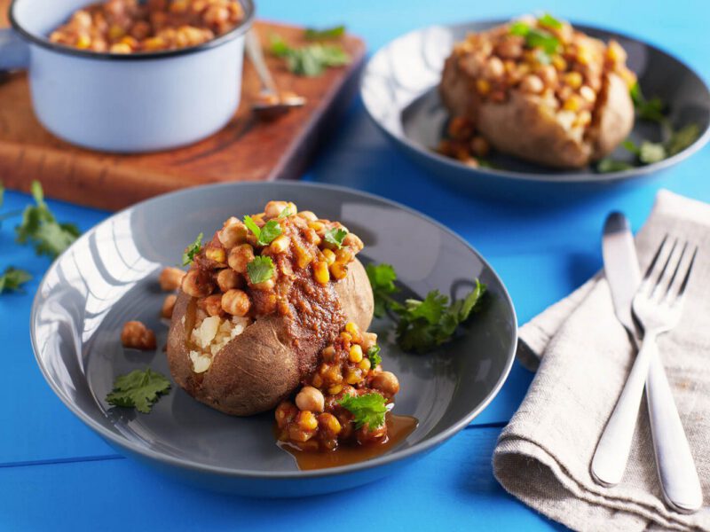 Two servings of Vegan Chickpea Chili on Baked Potatoes served in wide-mouthed bowls with a pot of Chickpea Chili in the background