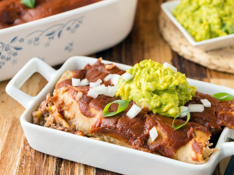 Bean & Corn Enchiladas topped with guacamole and sliced green onions