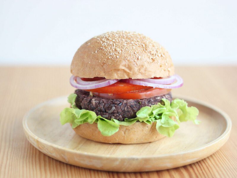 One veggie burger, with lettuce, a veggie pattie, and tomato and red onion slices on a whole grain bun. On a wooden plate