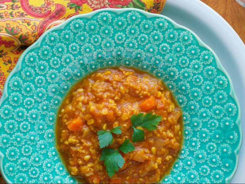 A top-down shot of Moroccan Lentil Soup in a turquoise bowl with a colorful red and yellow cloth napkin beside the bowl