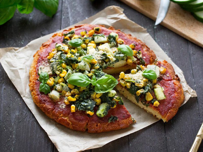 Chickpea Flour Pizza Crust (Gluten-Free) on parchment paper on a wooden table top with fresh basil and tomato to the side