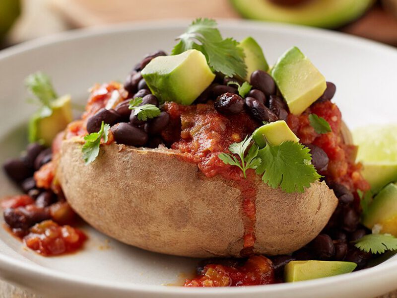"Nacho" Vegan Baked Potato on a white plate with a garnish of slices of avocado and cilantro