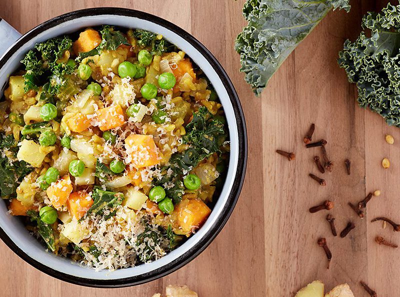 Vegan Kichadi on a wooden table with fresh cloves and kale