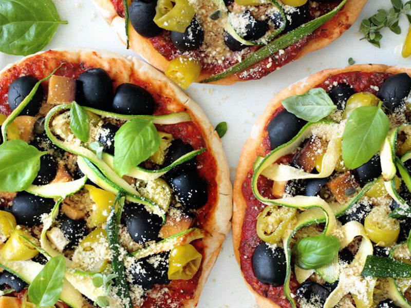 Three Vegan Pita Pizzas on a round marble chopping board