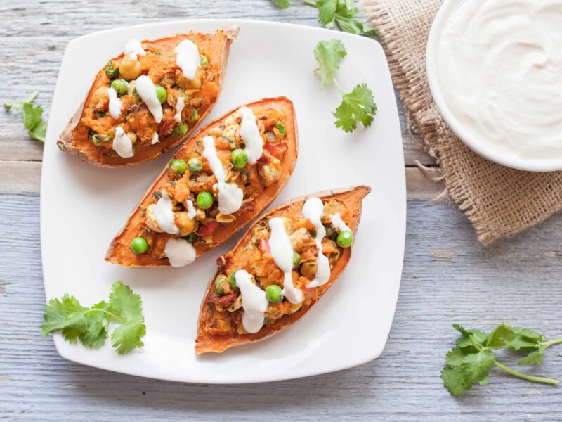 Twice-Baked Sweet Potatoes on a white plate, next to a bowl of vegan sour cream with cilantro dotted around