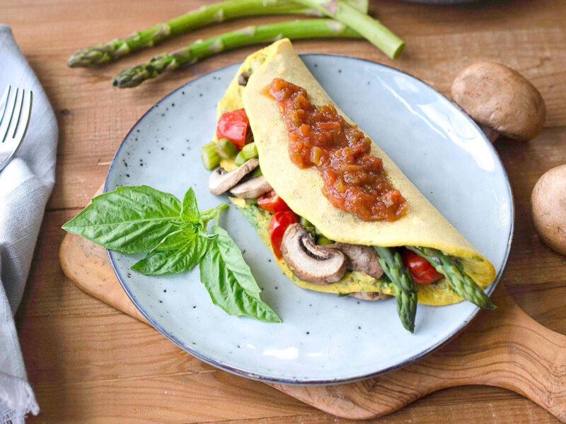 Leftover Veggie Chickpea Omelette topped with salsa on a blue plate with a sprig of basil