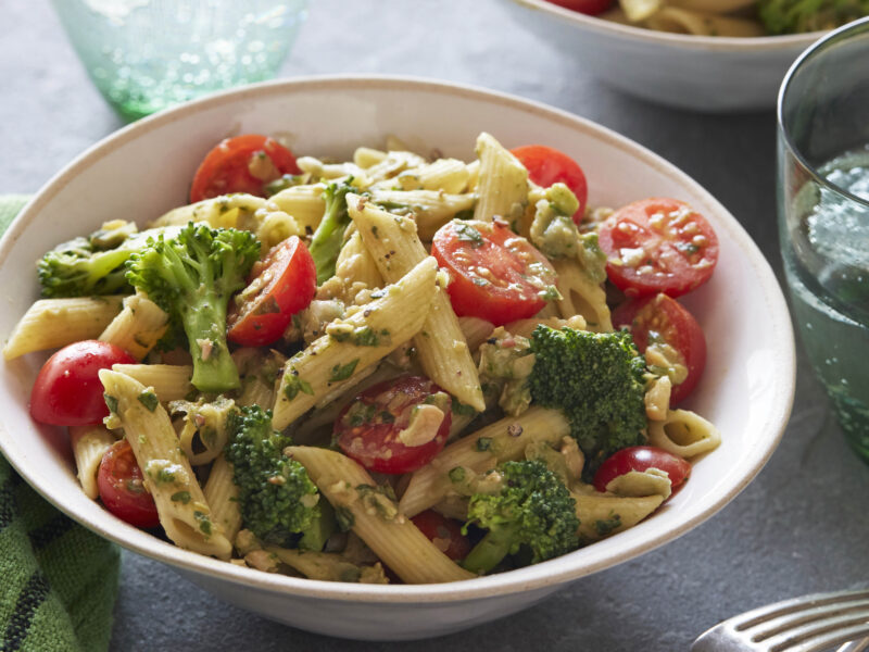 Pesto Penne in a white bowl next to a glass of water