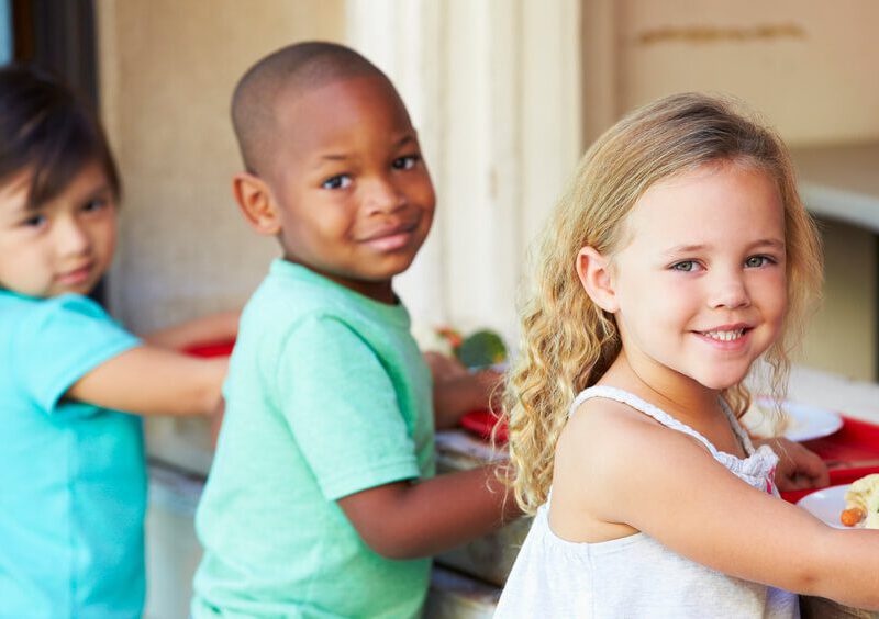 Three Elementary Pupils Collecting Healthy Lunch In Cafeteria