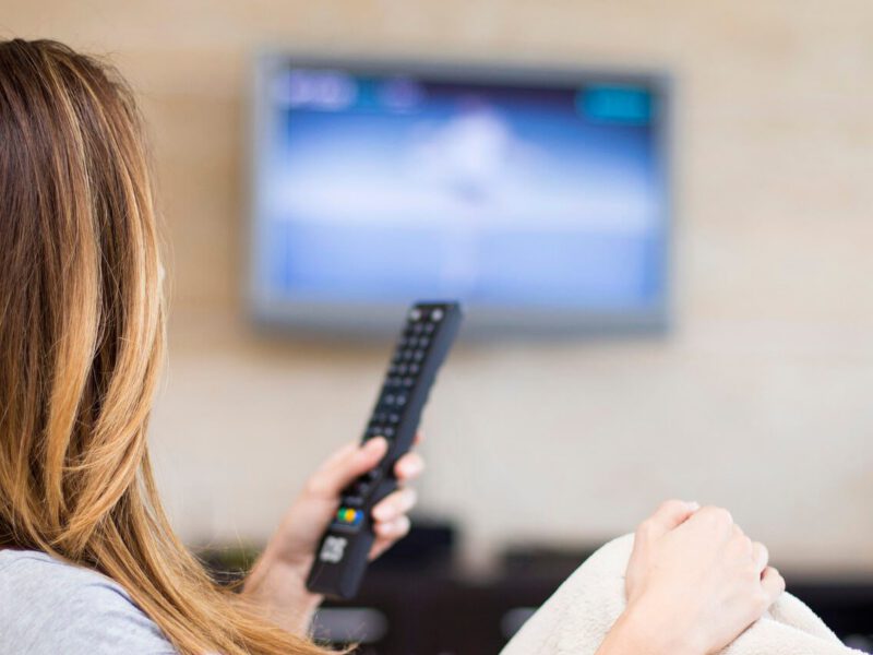 The back view of a woman holding a remove looking at TV screen in the distance