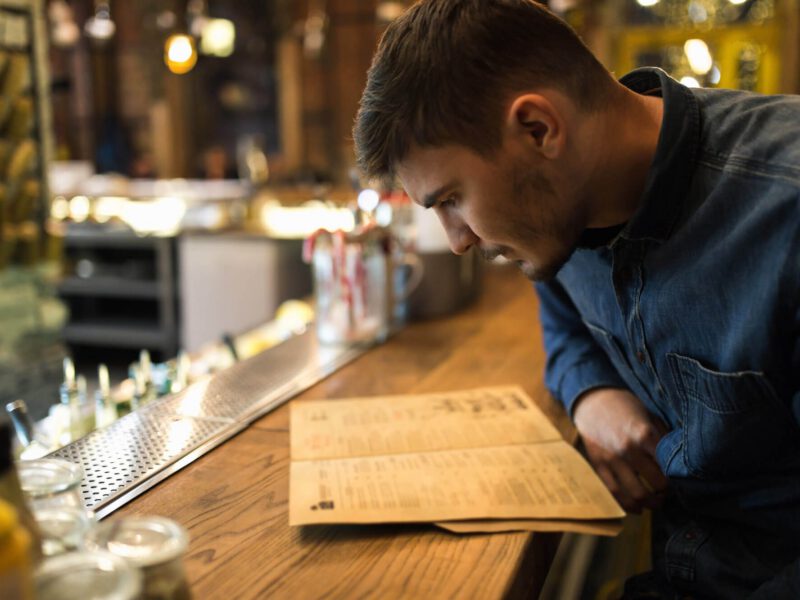 A young man sitting at a bar, looking intently at a dinner menu