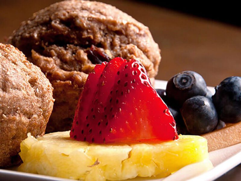 Two muffins on a plate with a disc of pineapple, fresh strawberries and blueberries, ready for Mother's Day