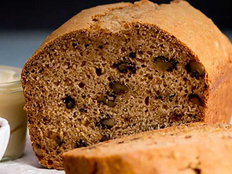A loaf of Apple-Walnut Breakfast Bread with one slice cut next to a small dish of raspberry jam